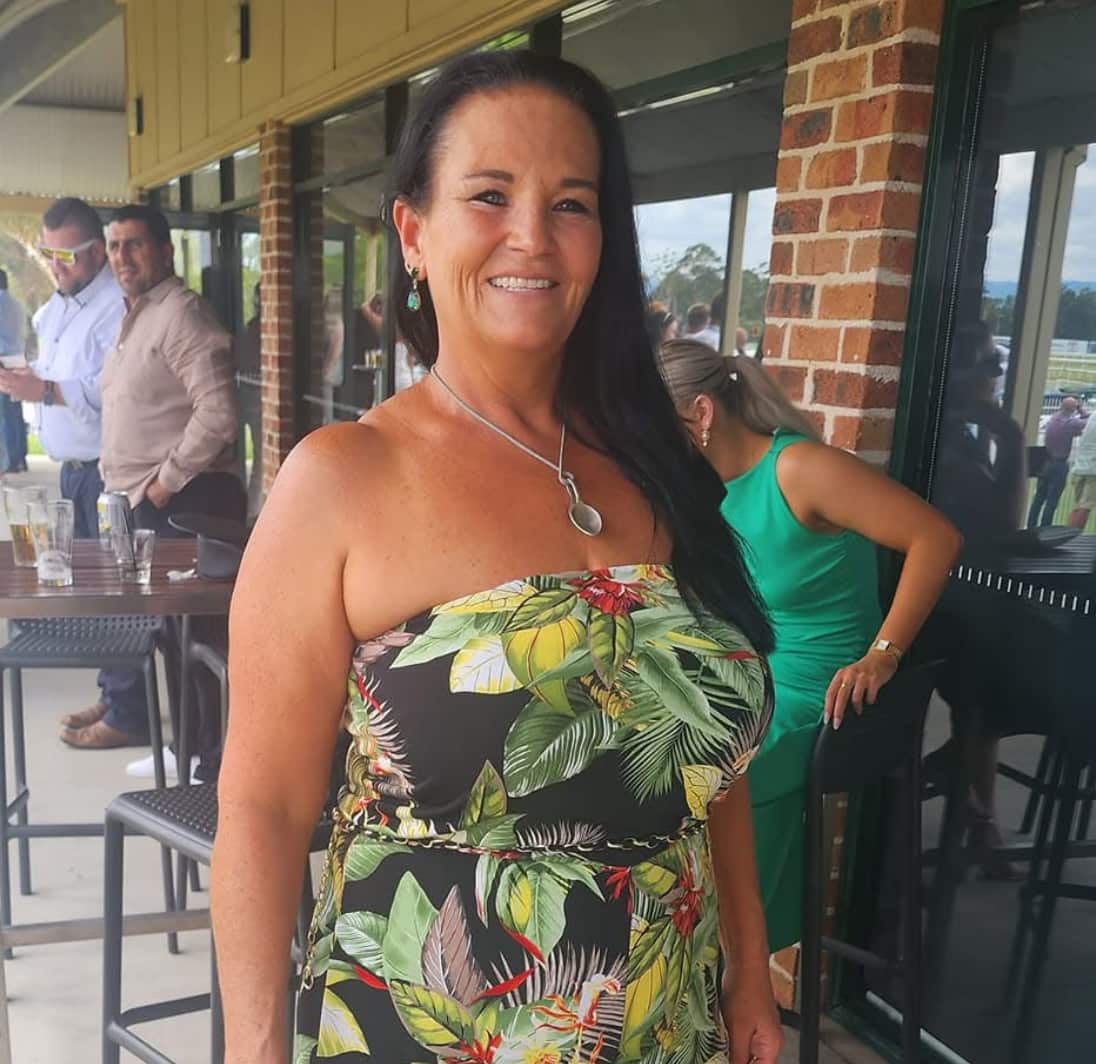 A middle-aged white woman smiling and a wearing a floral-patterned dress. 