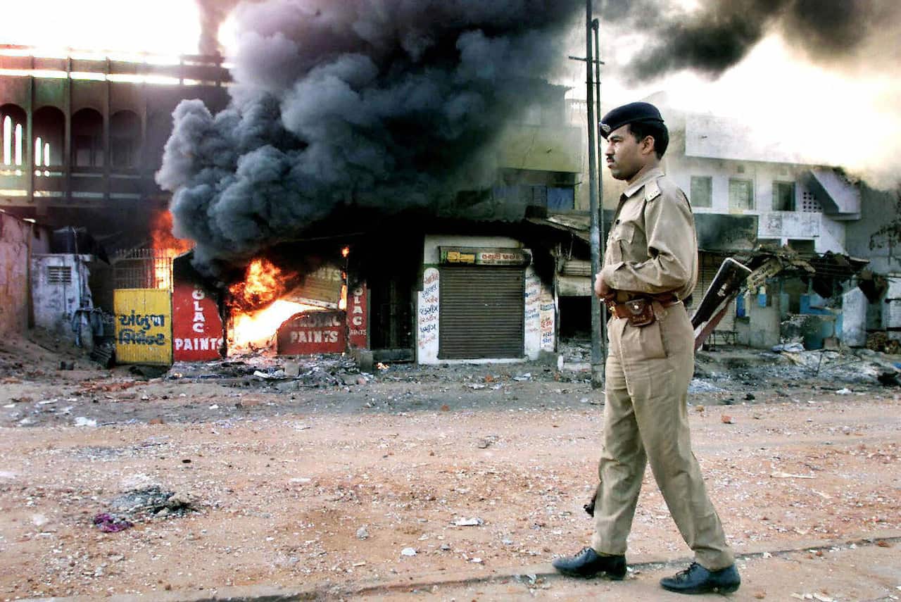 A policeman stands in front of burning building.