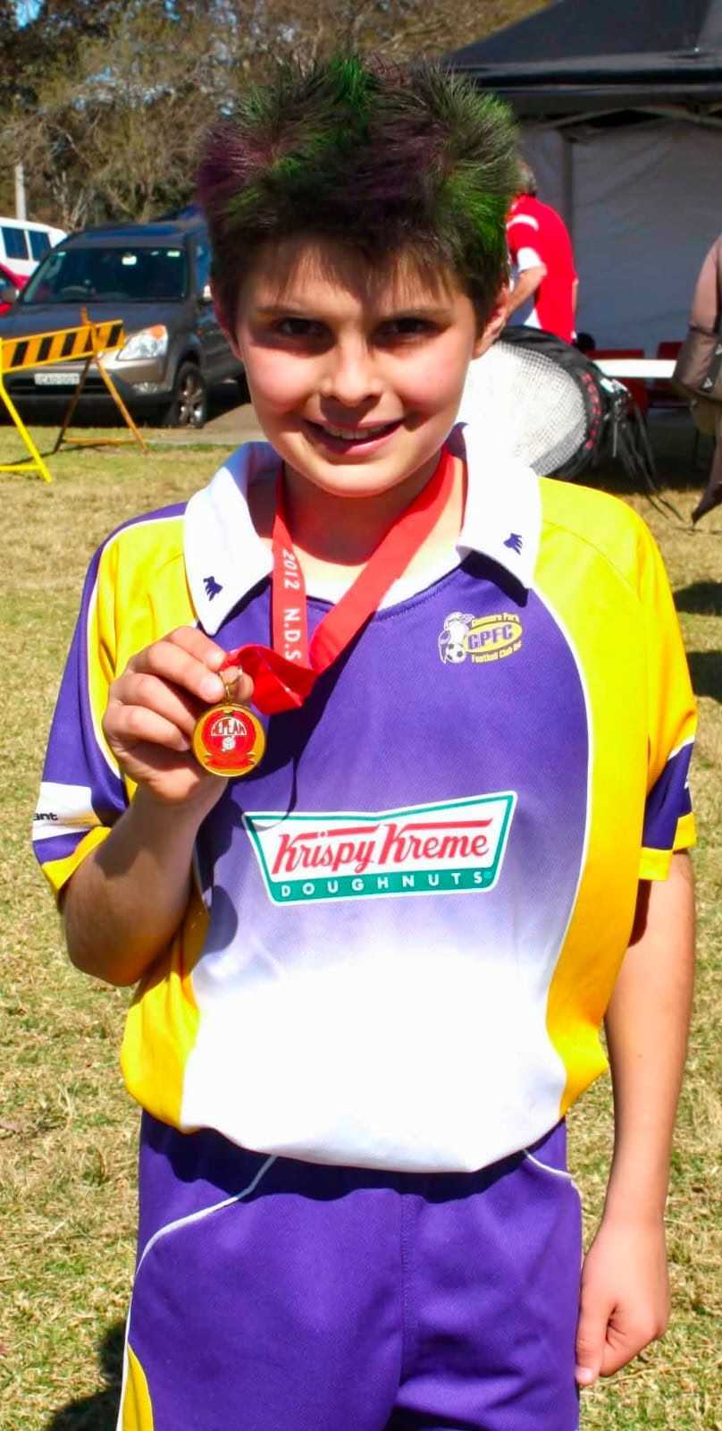 A young Patrick Beach holds his medal up to the camera at a weekend soccer comp