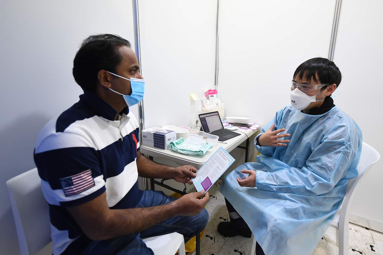 A man speaks with a healthcare worker holding a pamphlet at a vaccination clinic. 