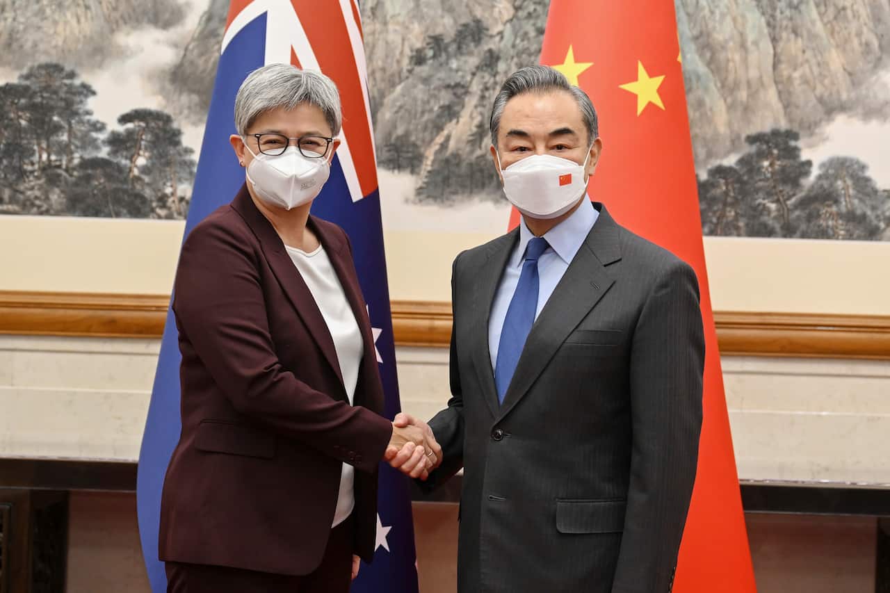 A woman wearing a suit and face mask shakes hands with a man wearing a suit and face mask 