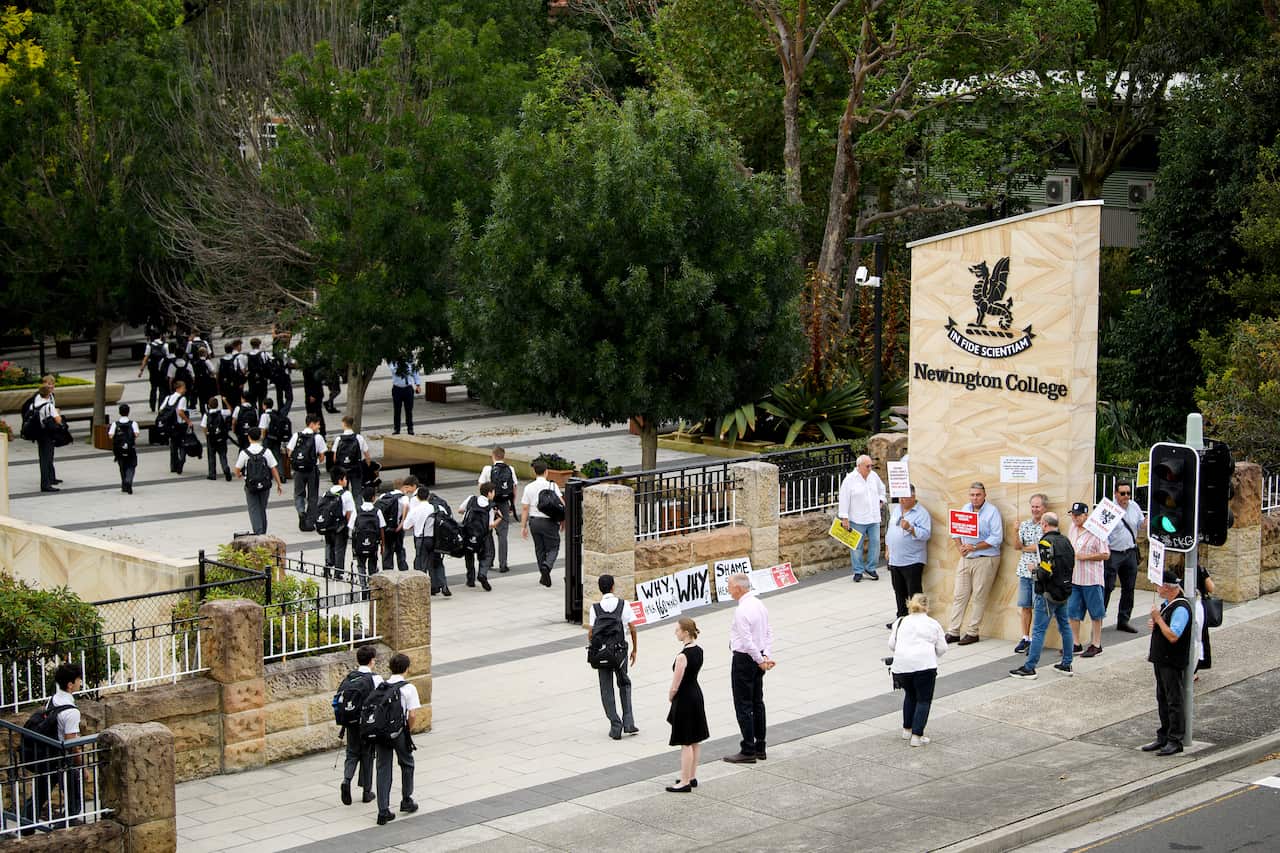 Students entering through a school gate where some people are protesting.