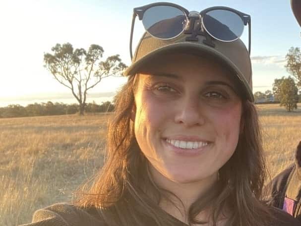 A woman with brown hair standing in a paddock smiling
