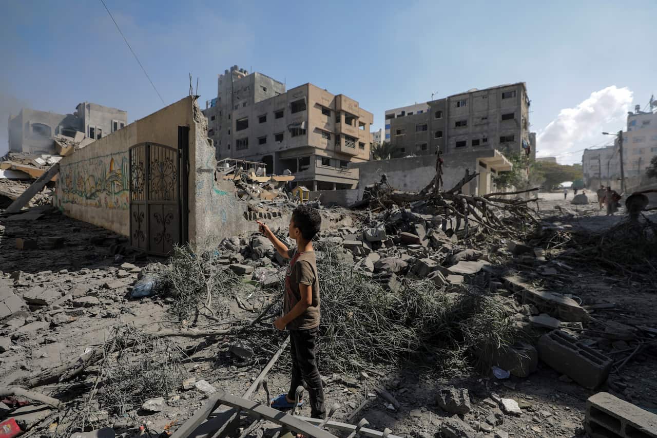 A young boy standing amid rubble looking out at destroyed buildings.