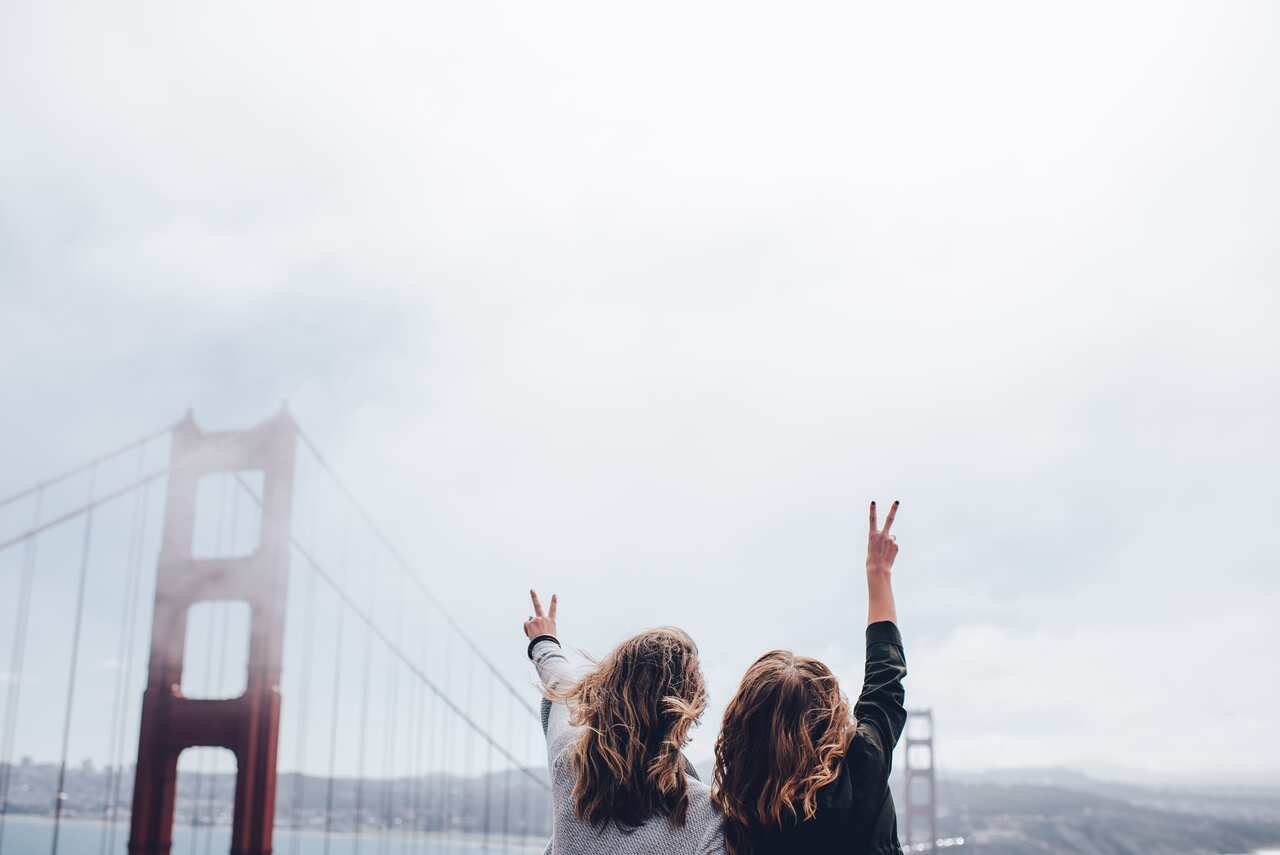 Two women with the back of their heads to the camera arms raised with two fingers held up on their hands