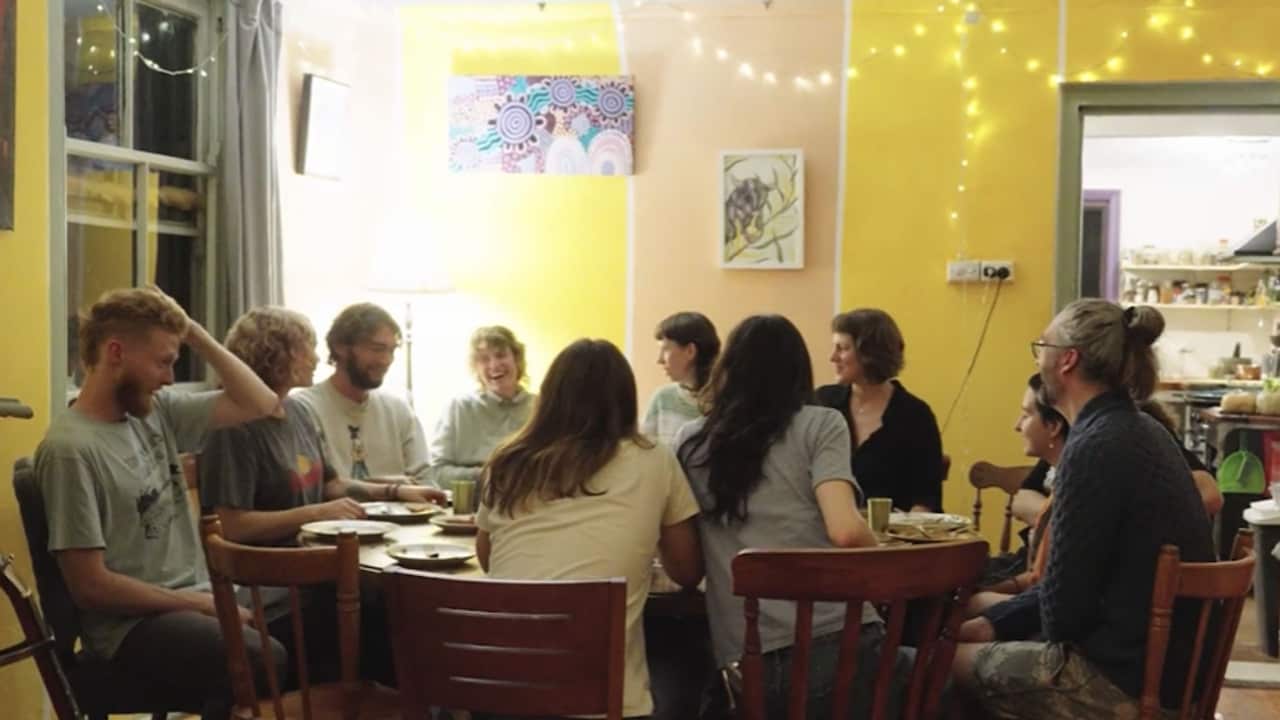 a group of people sitting around a dinner table. the walls are yellow with fairy lights strung on them