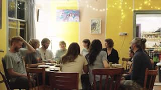 a group of people sitting around a dinner table. the walls are yellow with fairy lights strung on them