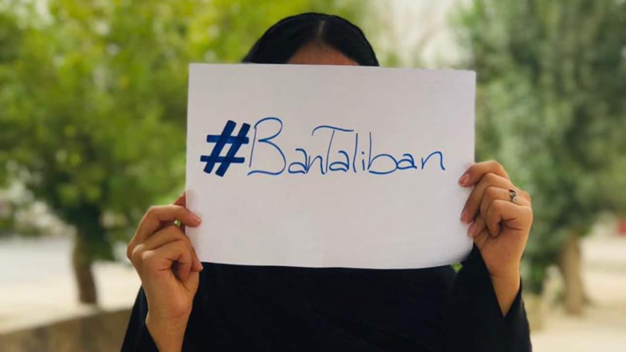 Woman holds a piece of paper bearing the words "#BanTaliban" in front of her face.