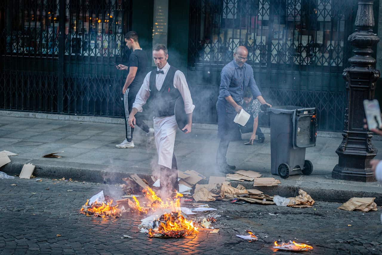 Two men put out a fire set by demonstrators as a third man walks by in the background.