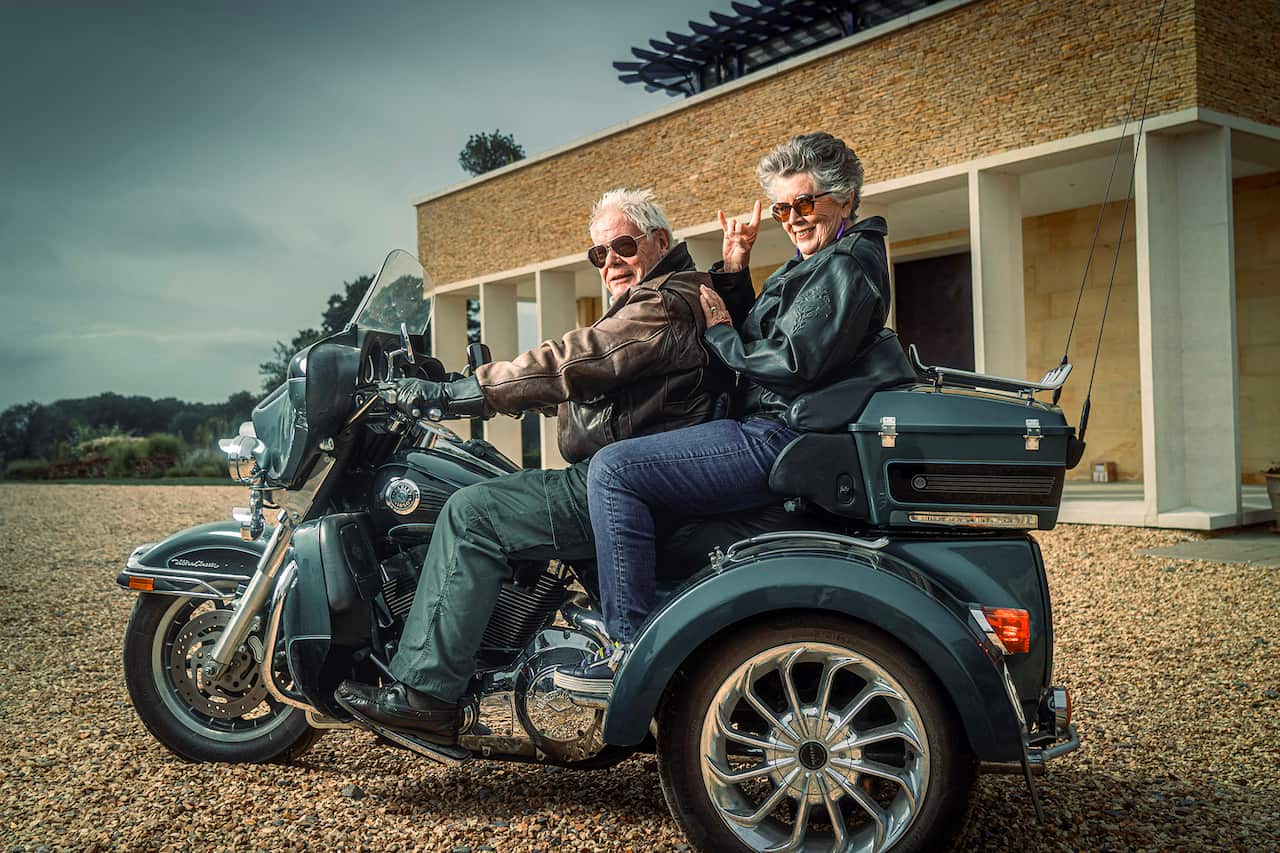 A man and a woman sit on a Harley outside a house. 