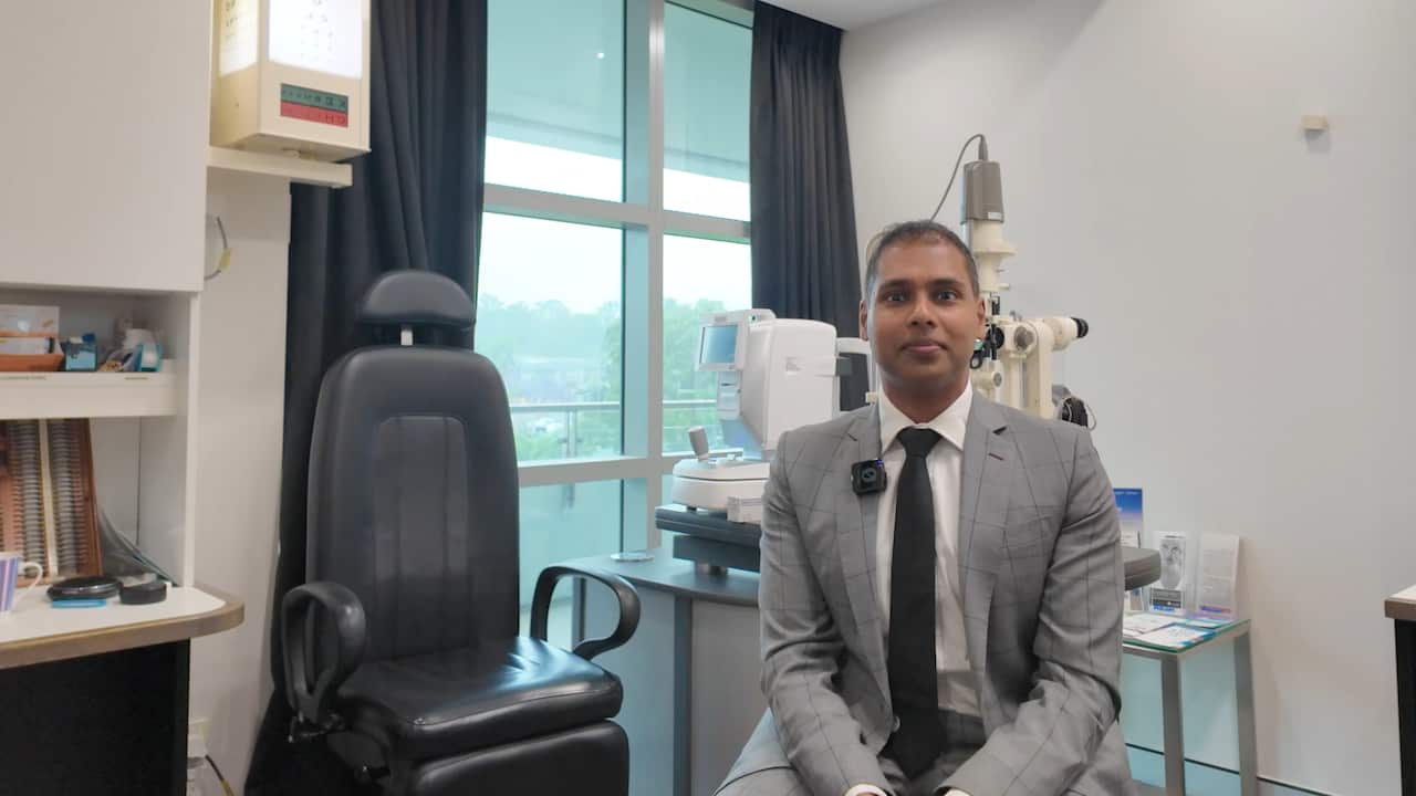 A man in a grey suit sitting in an office chair in an ophthalmology clinic room