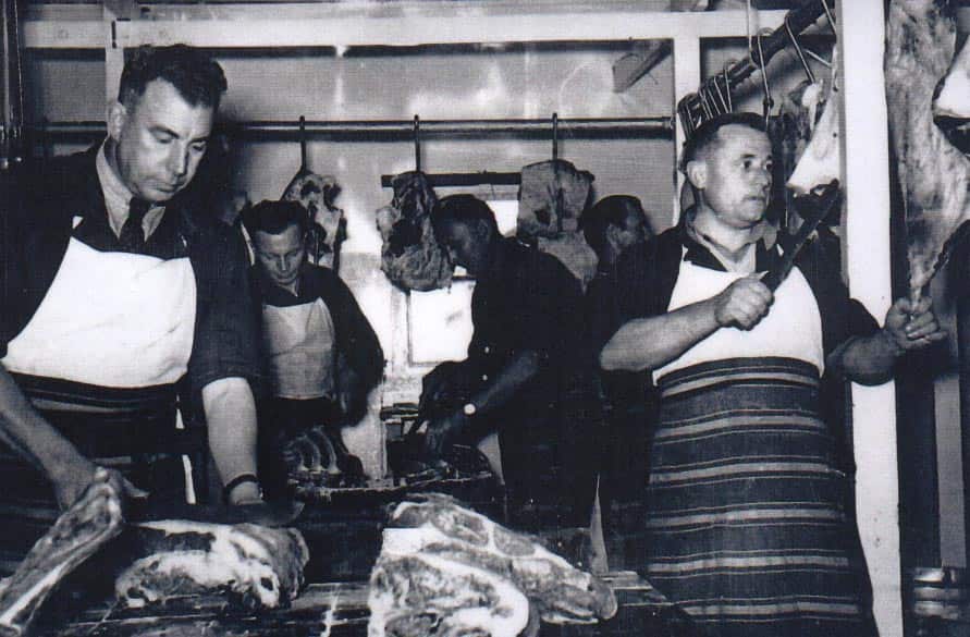Butchers hold knives surrounded by meat
