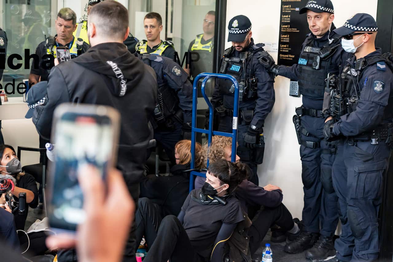 Police officers standing around protesters who are seated on the ground.