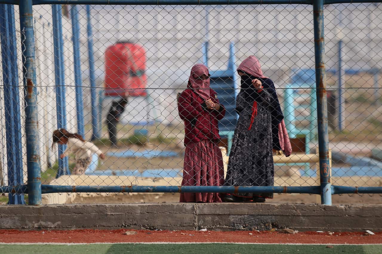 Two women in detention camp hold onto chainlink fence