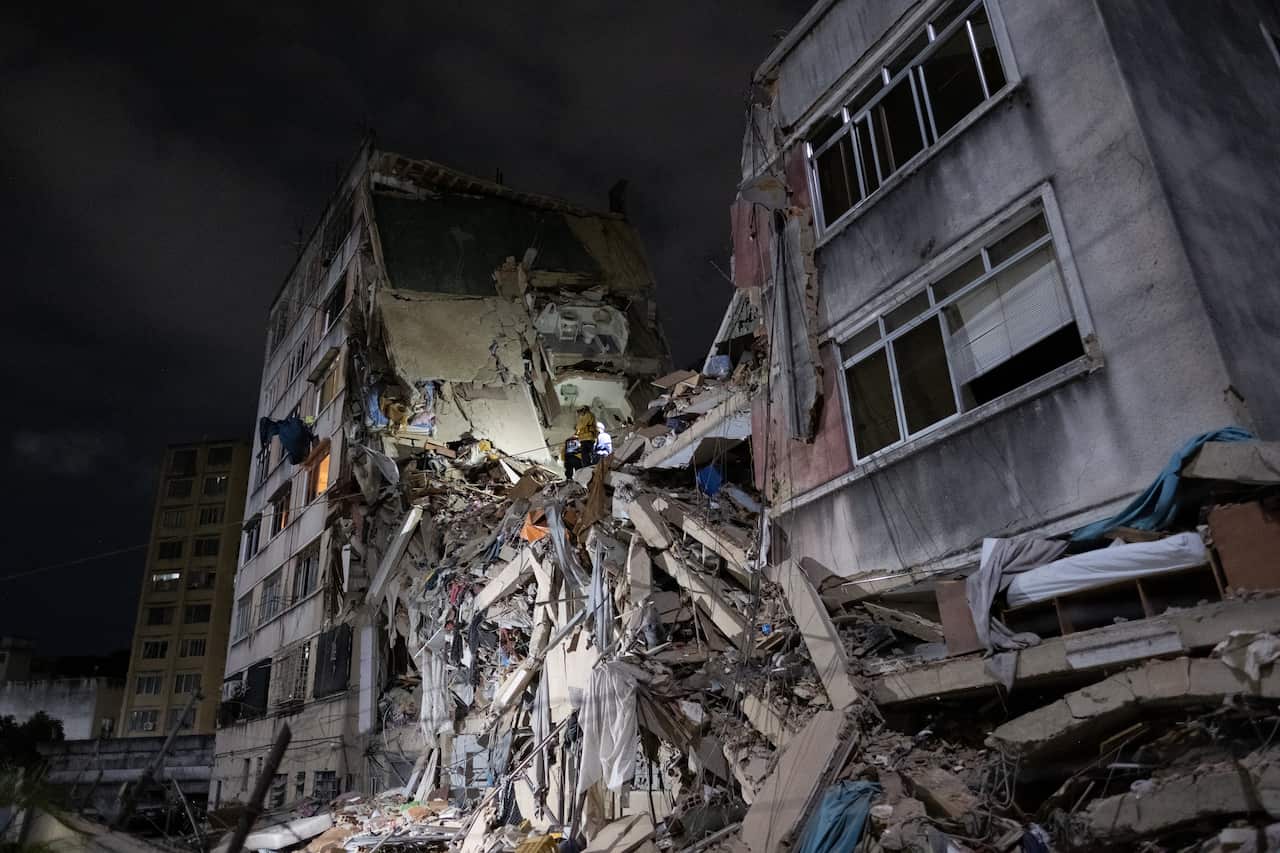A concrete building has collapsed in the middle and is illuminated at night.