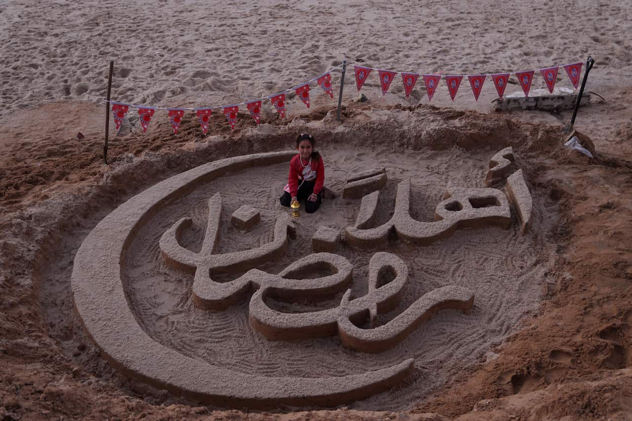  'Welcome Ramadan' written in Arabic in the sand with young girl sitting in the middle.