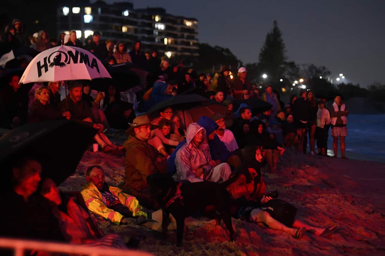 A large crowd of people sitting on rocks on a shoreline.