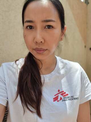 A doctor in a white shirt with the "Medicins Sans Frontieres" logo and long black hair in a ponytail.