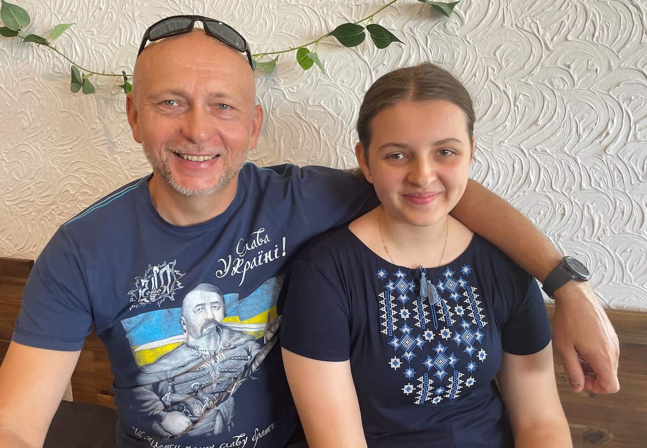 A man sitting with his arm across the shoulder of his daughter