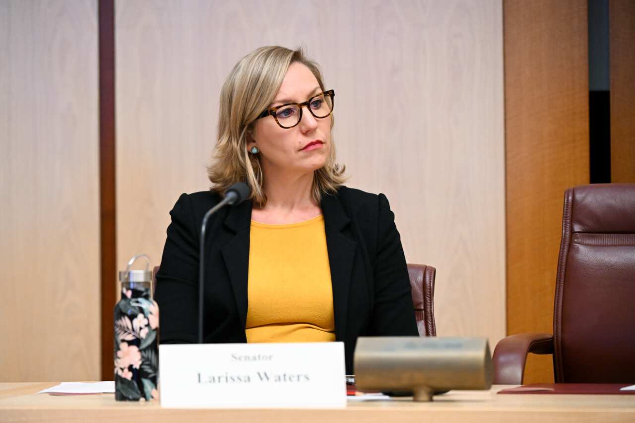 Woman in black blazer and yellow t-shirt sitting behind a desk 