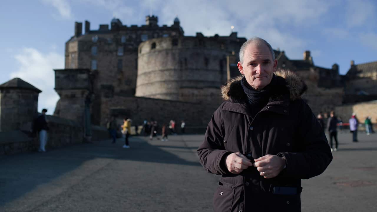 A man stands in front of a castle. 
