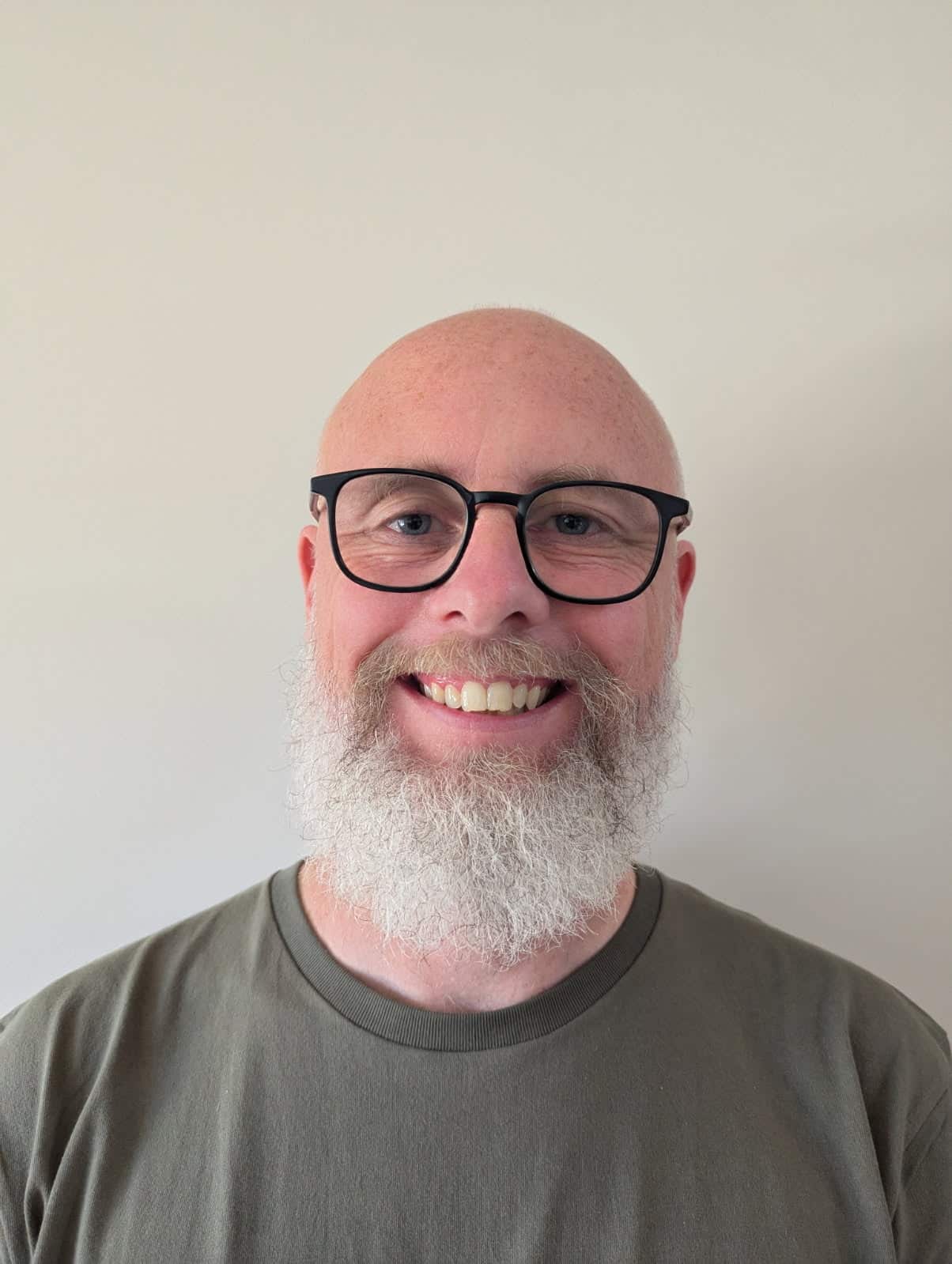 A man wearing glasses smiling against a white wall.