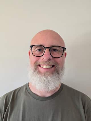 A man wearing glasses smiling against a white wall.