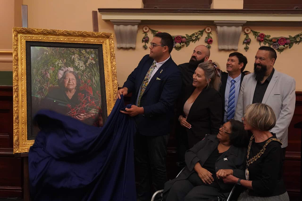 A group of people react as a portrait is revealed