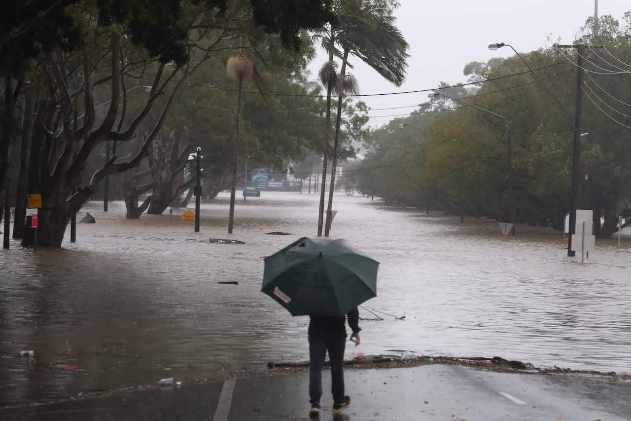 A person with an umbrella looks out at a flooded street in Lismore