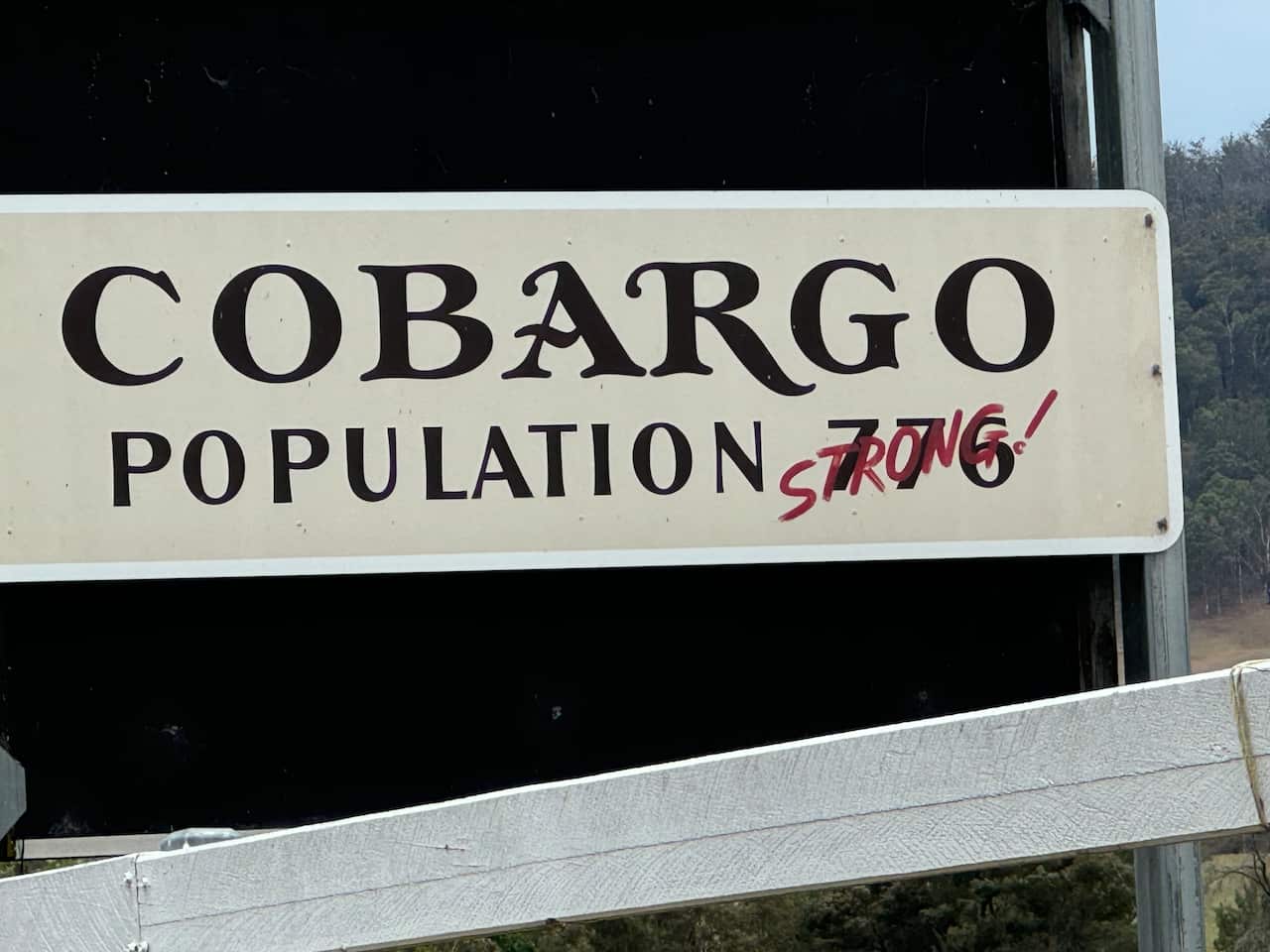 A sign that reads 'Cobargo, population 776,' with the numbers crossed out and the word 'strong' written in red marker.