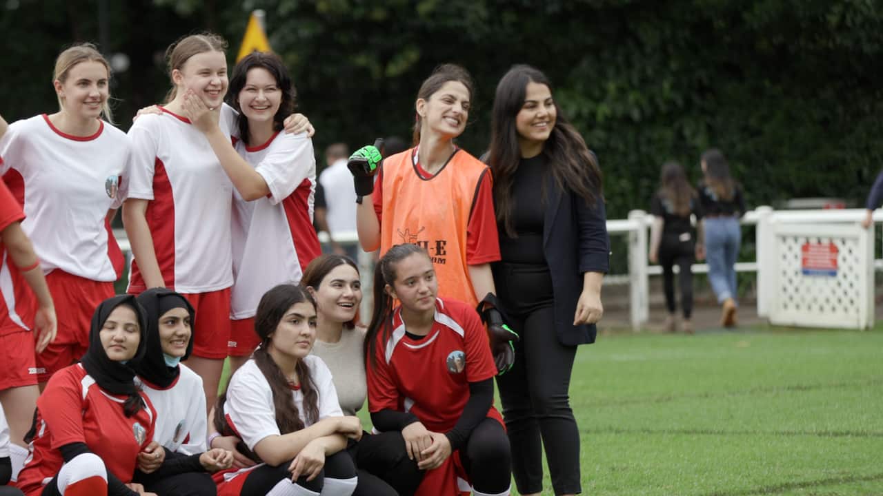 Newly arrived Afghan women and girls in soccer uniforms pose for a photo on a ground in Sydney.