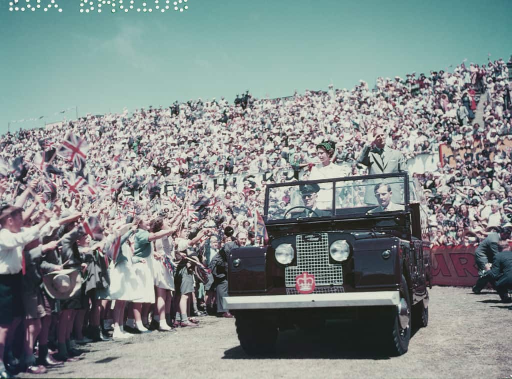 Queen Elizabeth and Prince Philip stand in the back of a Land Rover jeep and greet crowds in Australia in 1954