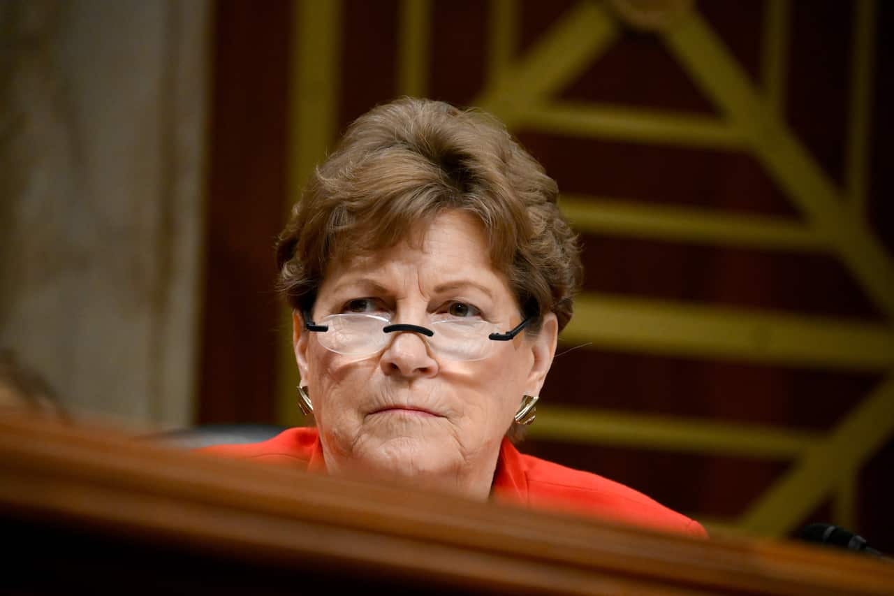 A woman wearing a red top and glasses inside.