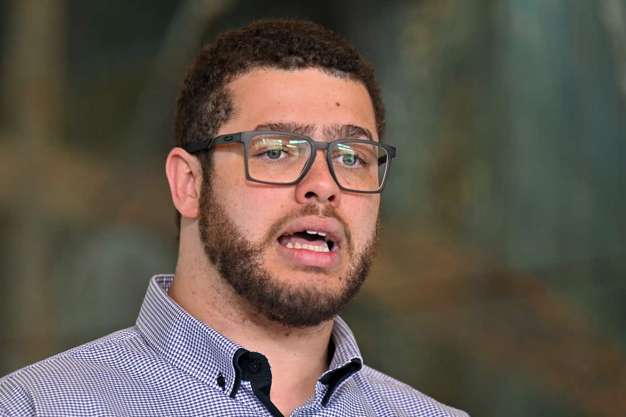 A man in a blue check shirt and glasses is speaking. 