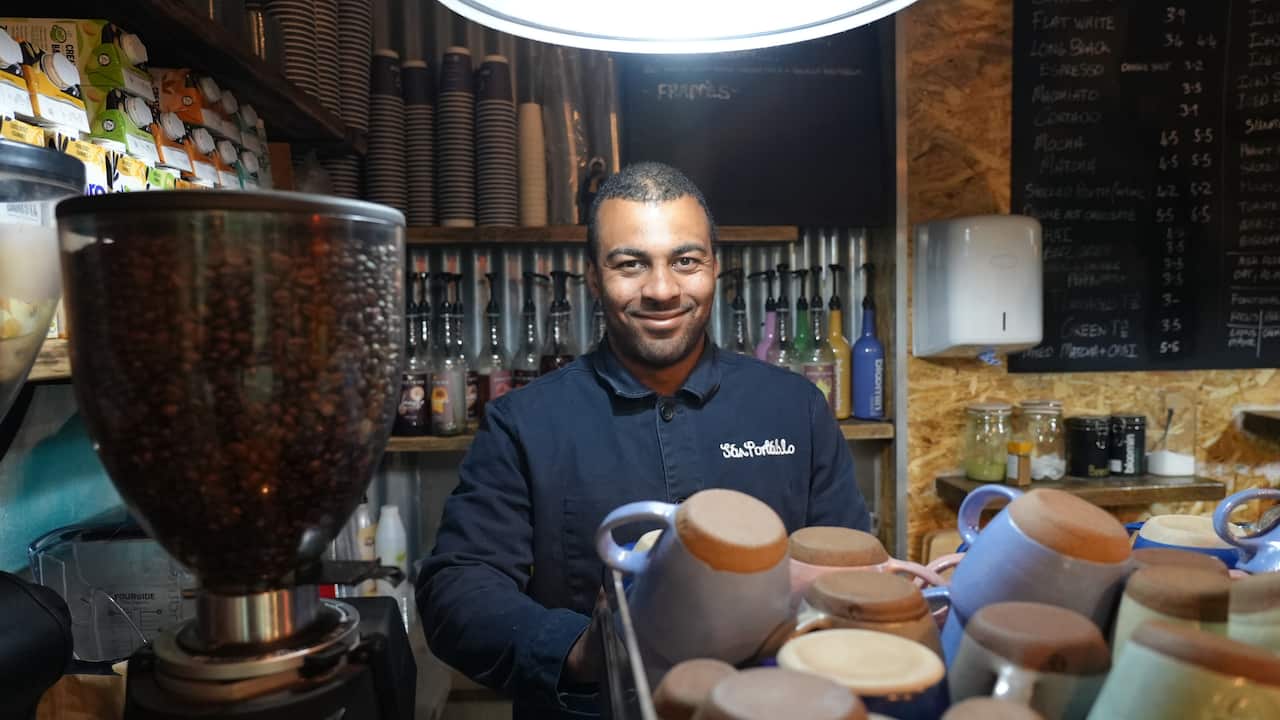 Cassius Walker-Hunt at work in his cafe, surrounded by mugs and a coffee machine filled with beans.