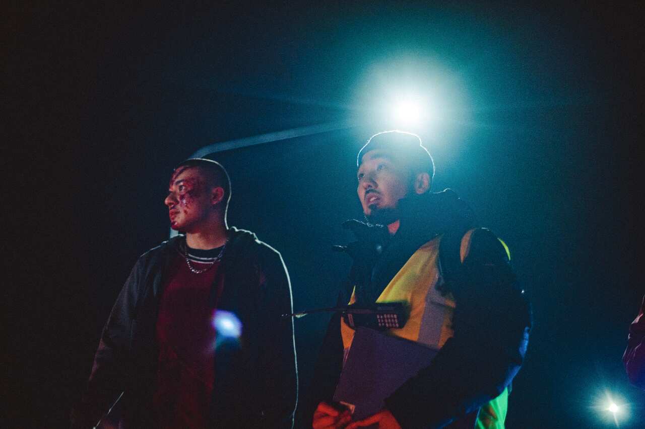 Two men stand in the dark, one in a hi-vis vest. 