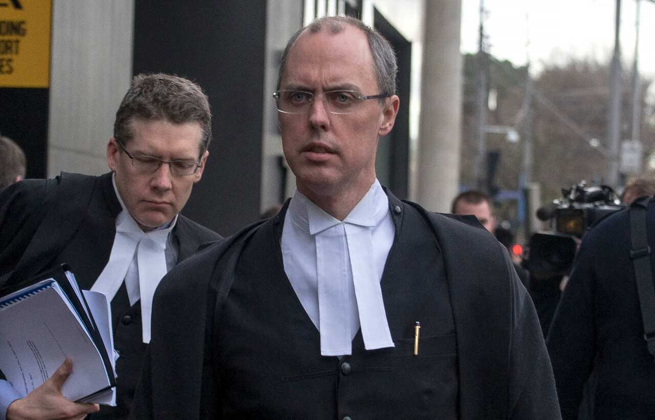 A man wearing formal legal attire stares forward.