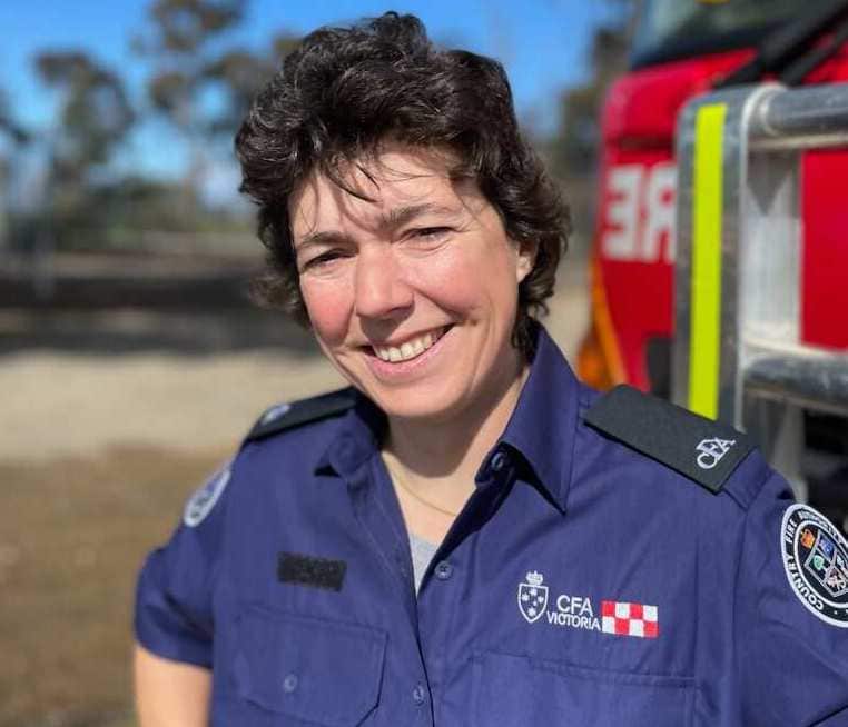 A woman dressed in a blue uniform stands in front of a red fire truck