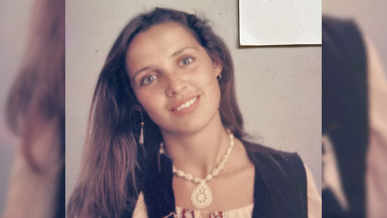 a young woman in overalls with long brown hair and wearing a shell necklace
