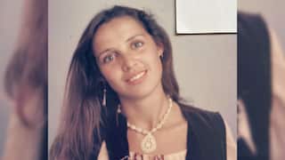 a young woman in overalls with long brown hair and wearing a shell necklace