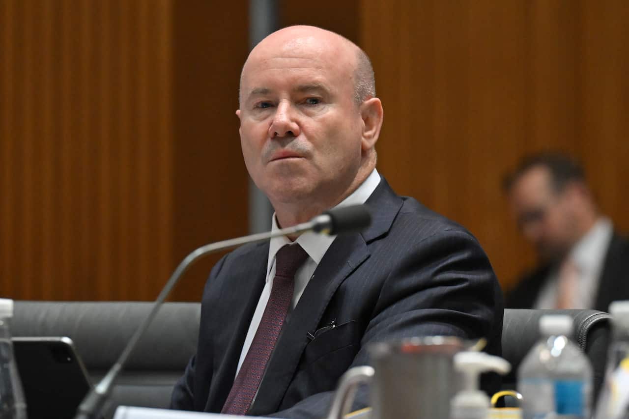 A man in a suit looks at the camera with a serious expression.