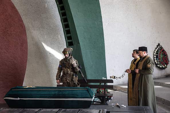 A Ukrainian soldier stands at the coffin of his father. To the right are two priests.