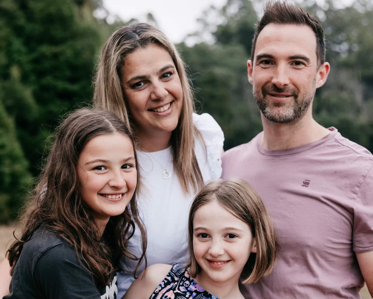 A family portrait of a mum, dad and their two daughters. They are all smiling.