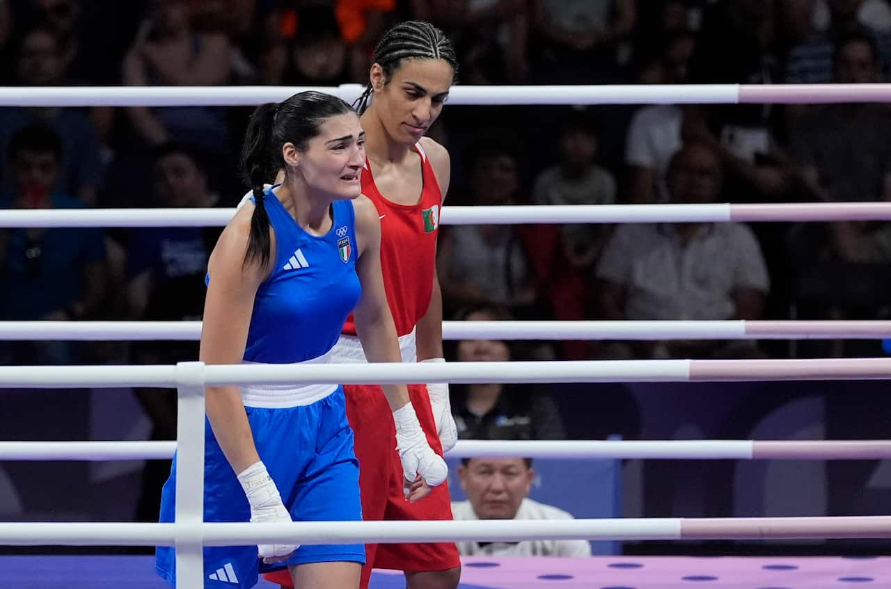 Two female boxers in the ring. One is in blue and the other is in red. The one wearing blue is in tears. 