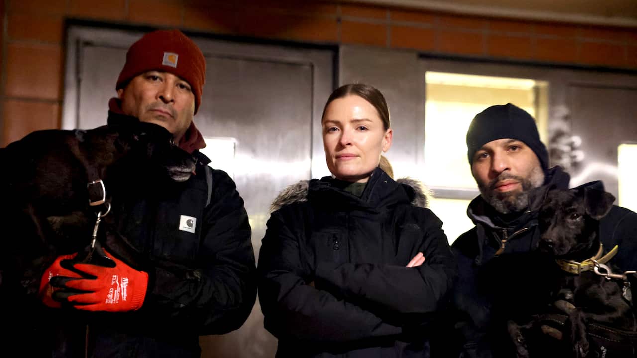 A woman standing between two men inside. They are all wearing black parkas