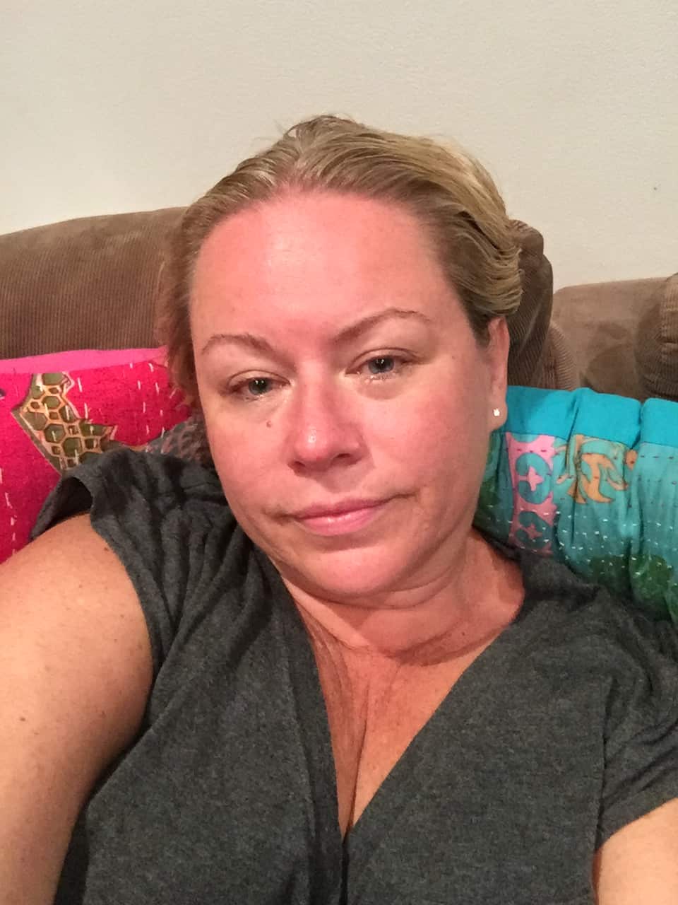 A woman sitting on a sofa full of colourful cushions looking at the camera with a neutral expression on her face.