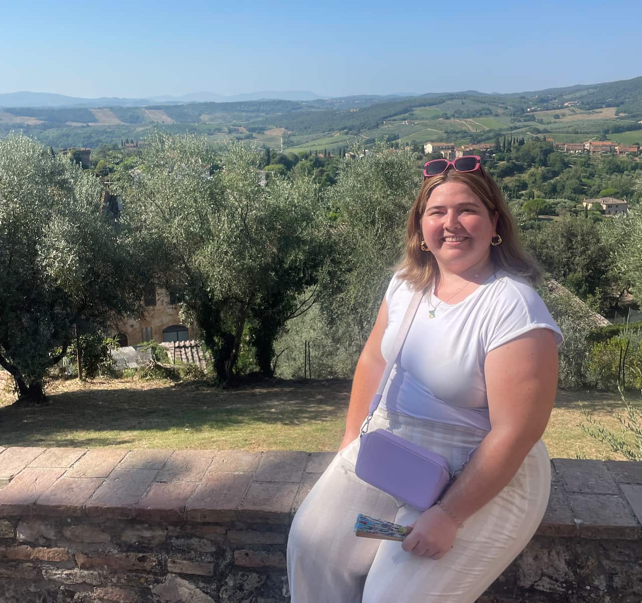 A young woman sitting on a brick wall smiling at a camera