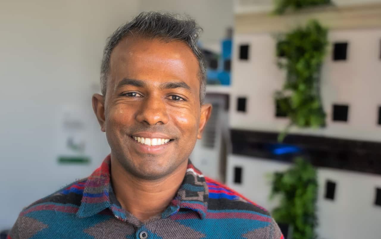 A man in a multi-coloured jacket standing in front of a decorative wall.