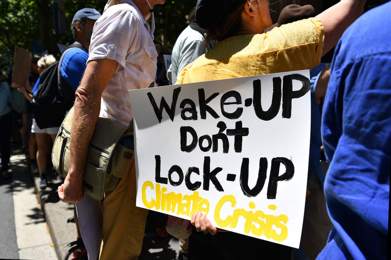 A protester holds a sign outside supporting climate action. The sign reads: "Wake up Don't lock up Climate Crisis."