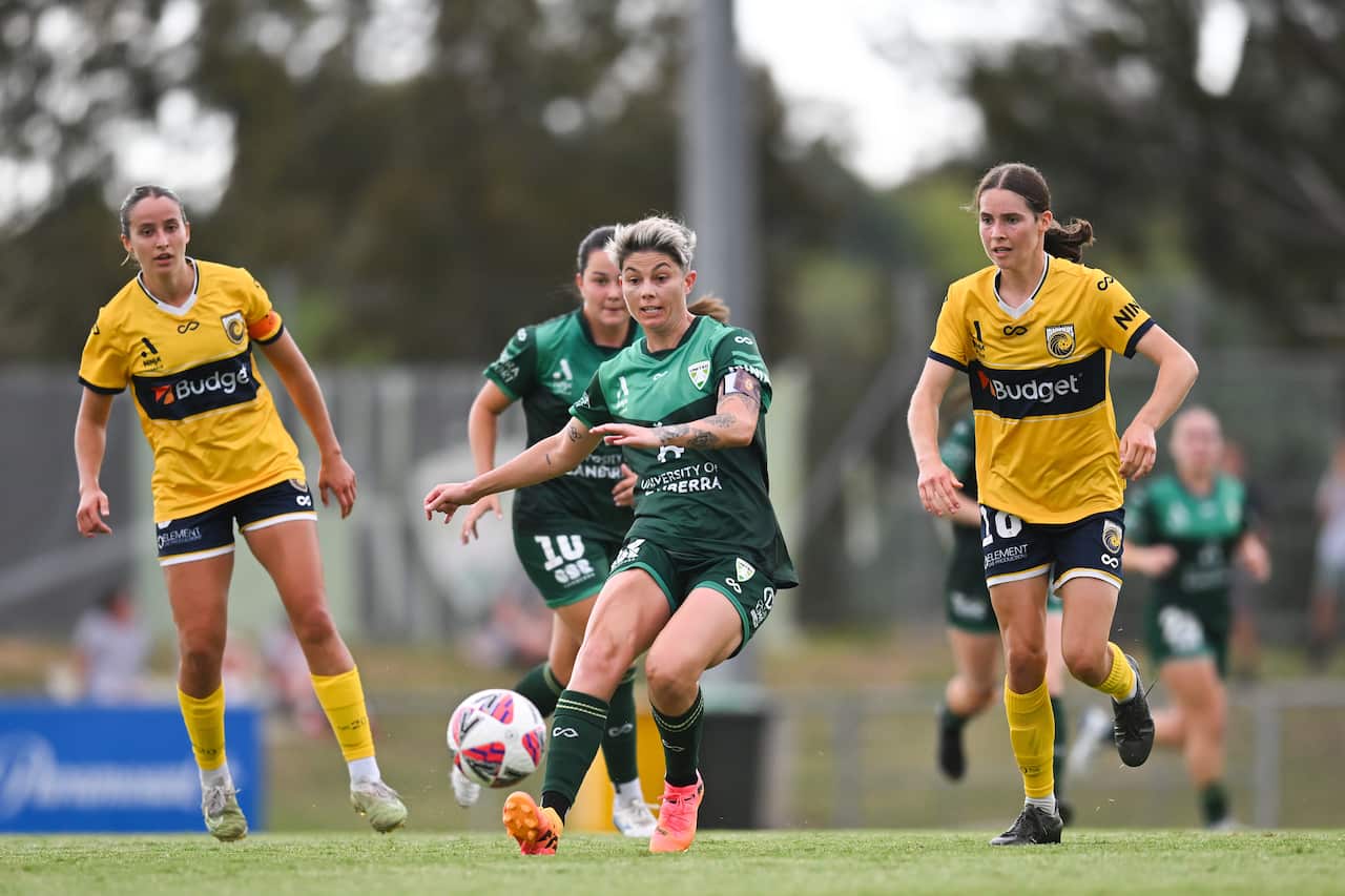 Two female football players in green kits are running in between two players in yellow and blue kits.
